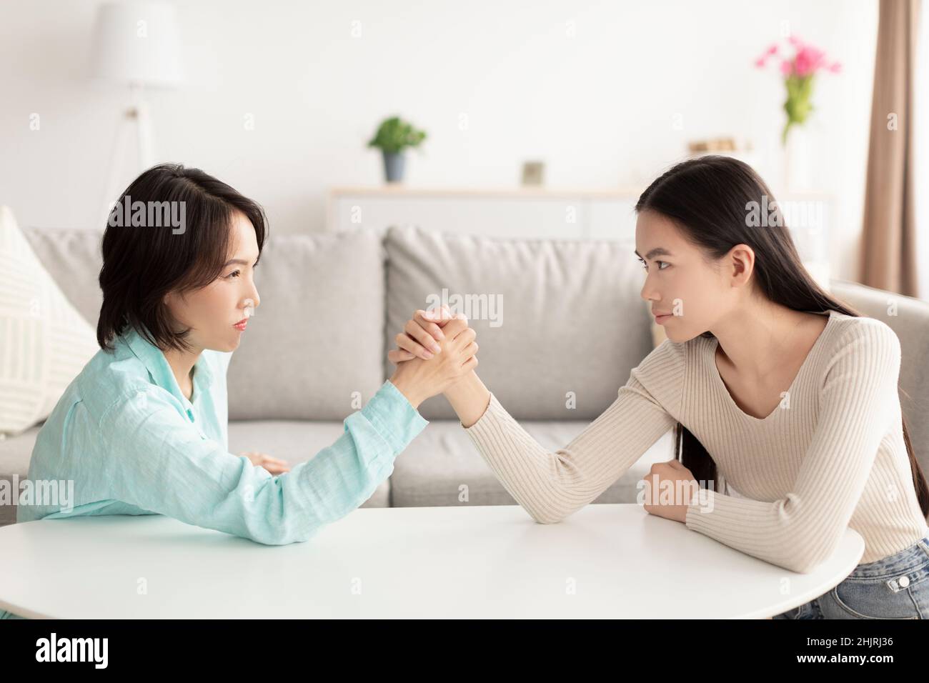 Reife asiatische Mutter und Erwachsene Tochter Arm Wrestling, einander in die Augen schauen, kämpfen zu Hause Stockfoto