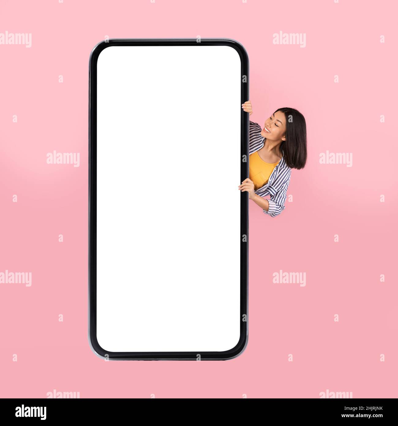 Asiatische Frau Versteckt Sich Hinter Großen Handy-Bildschirm Über Rosa Hintergrund Stockfoto