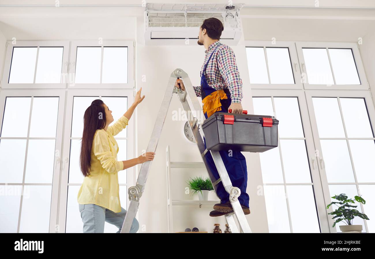 Techniker steigt mit seinem Werkzeugkasten auf die Leiter, um die Klimaanlage im Frauenhaus zu reparieren Stockfoto