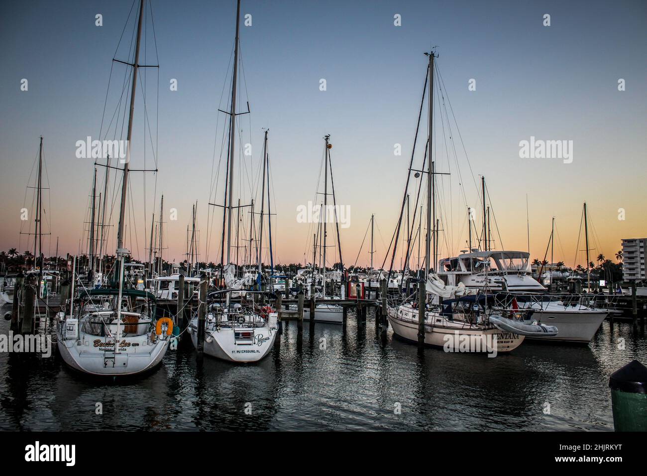 Der wunderschöne Sonnenuntergang im Hintergrund und alle Masten der hoch stehenden Boote. Das Wasser ist ruhig und reflektiert. Stockfoto