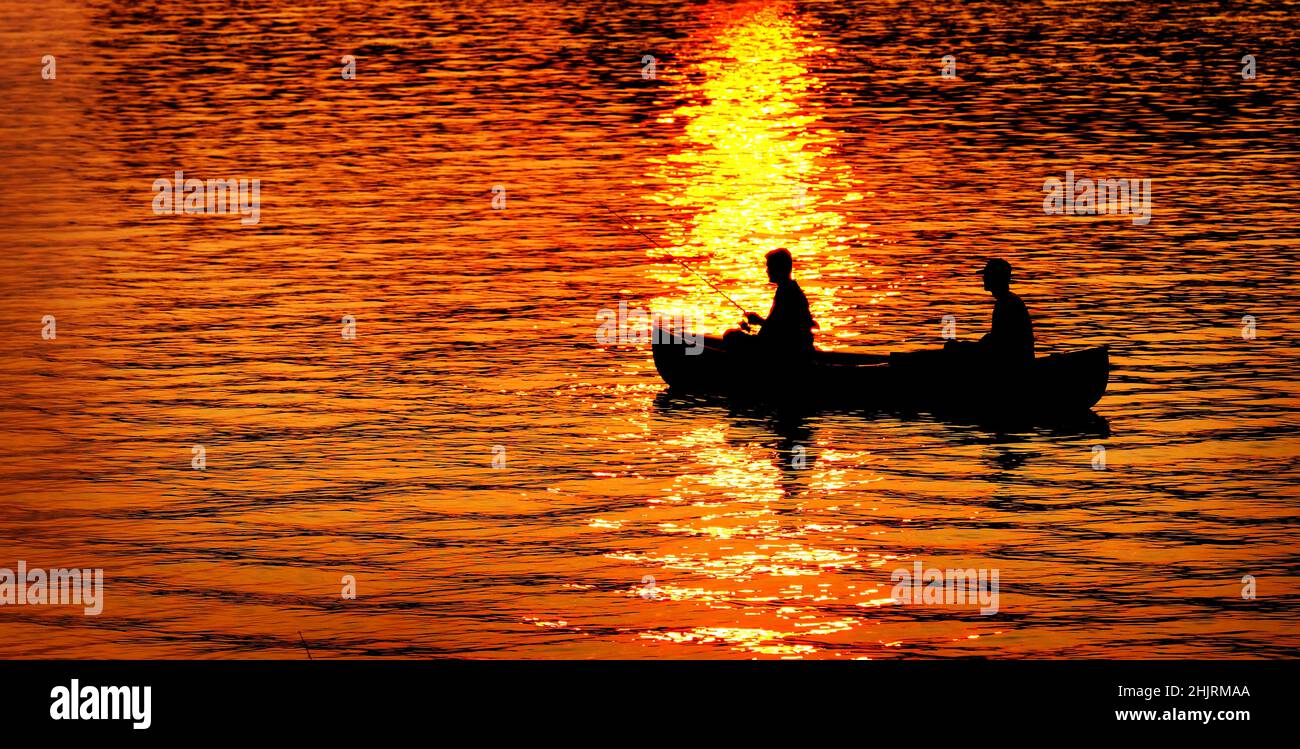 Zwei 2 Personen, die bei Sonnenuntergang bei Sonnenaufgang im See oder im Fluss angeln Stockfoto