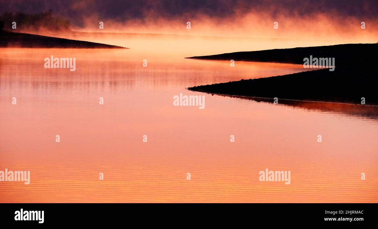 Nebliger Morgen auf dem See mit Dampf, der aus dem Sonnenlicht des Wassers aufsteigt Stockfoto