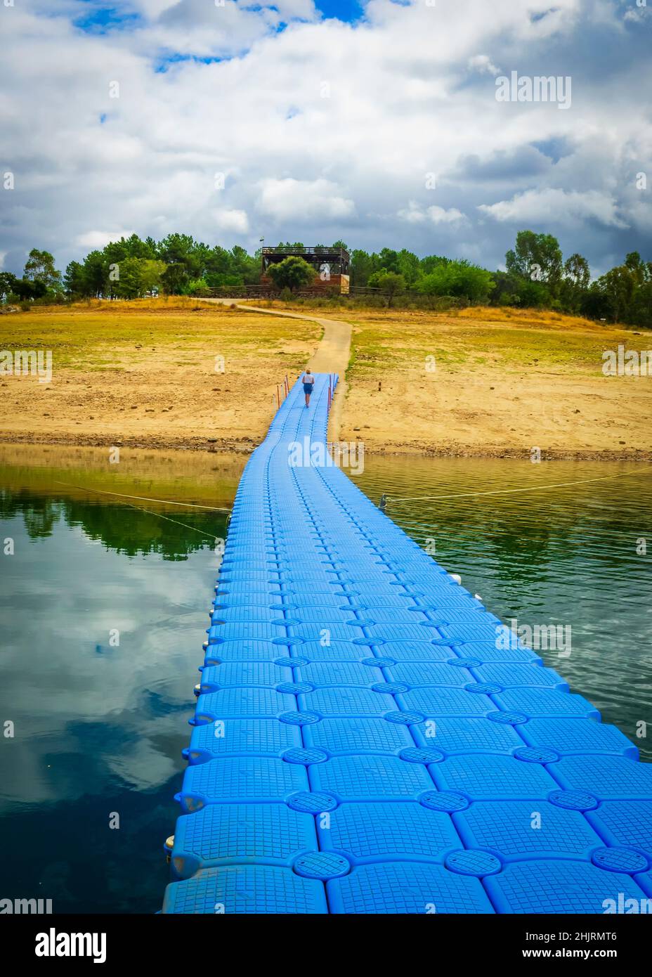 Eine einsame Frau geht am Ende eines blauen Docks am See spazieren. Stockfoto