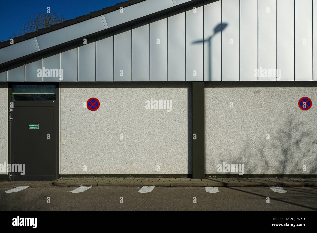 Der Schatten einer Außenleuchte an der Wand eines Gebäudes. Davor freie Flächen, die nicht als Parkplätze genutzt werden dürfen. Stockfoto