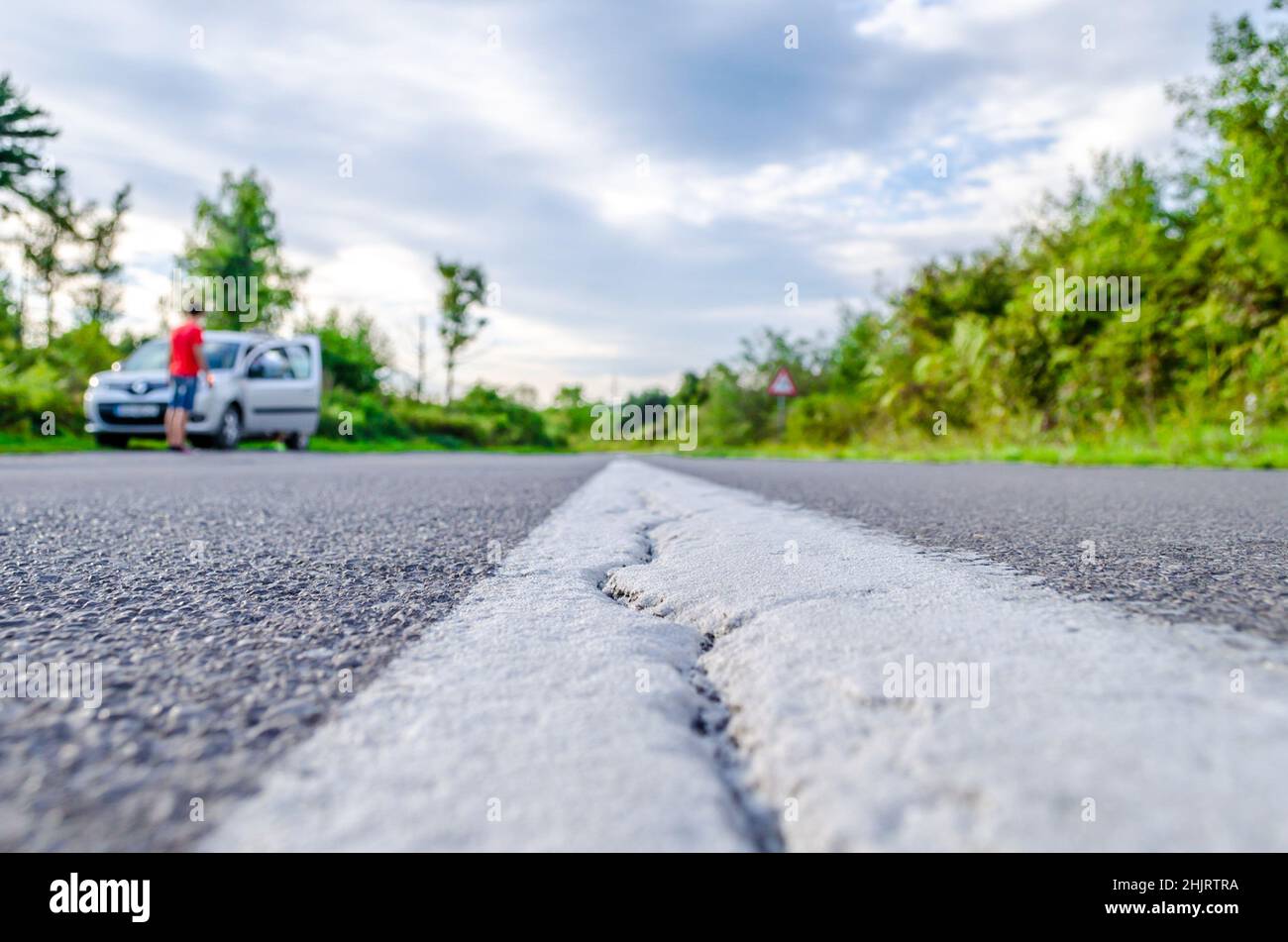 Gerade Asphaltstraße mit einem Crack auf der weißen Linie in der kroatischen Landschaft. Ein Fahrzeug hat zur Seite angehalten und die Menschen ruhen Stockfoto
