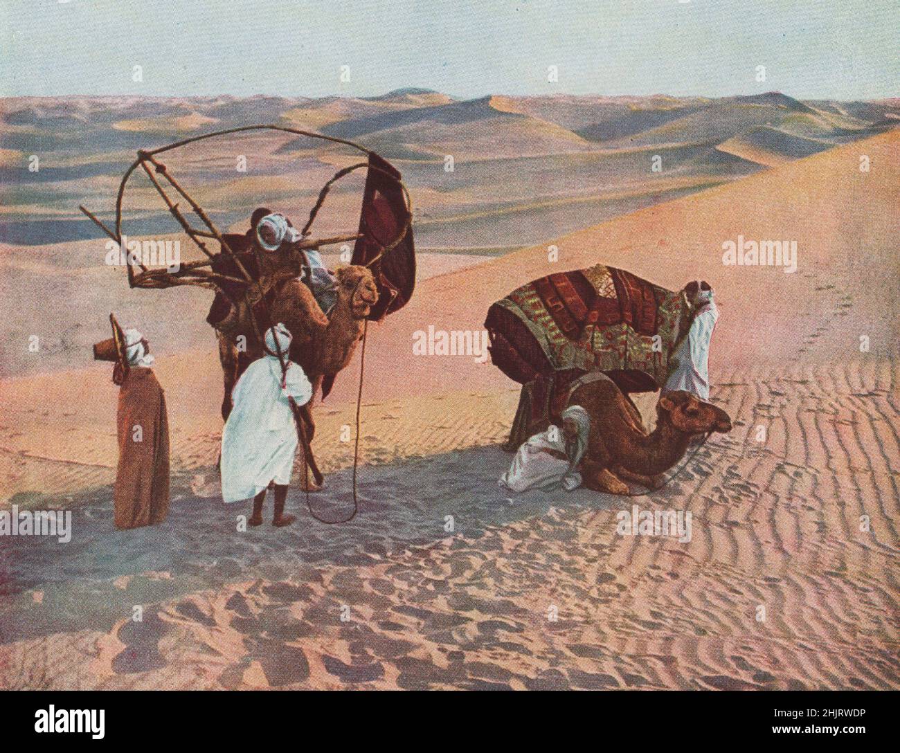 SAHARA. Während dieser Beduin seine Frauen-Leute durch den trostlosen Abfall begleitet, trägt er eine langarrelierte Waffe mit antikem Design. Nordafrika (1923) Stockfoto