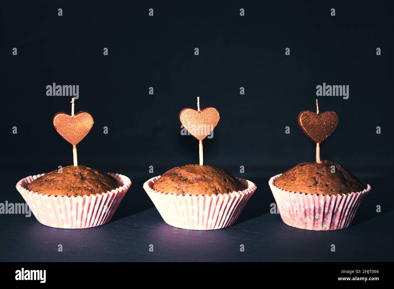 Schokoladen-Muffins mit herzförmigen Kerzen auf schwarzem Hintergrund. Postkarte zum Geburtstag oder valentinstag. Stockfoto