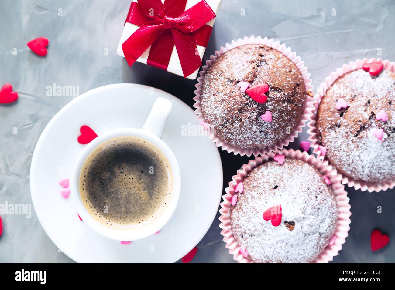 Tasse Kaffee, Schokoladenmuffins und Geschenk auf grauem Hintergrund. Das Konzept eines romantischen Morgens, Geburtstages oder valentinstag. Stockfoto