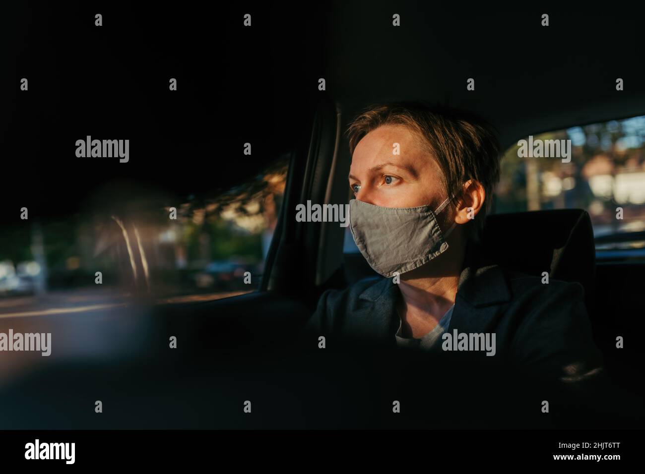 Besorgte Geschäftsfrau mit schützender Gesichtsmaske wartet im Auto und schaut aus dem Fenster, selektive Fokus Stockfoto