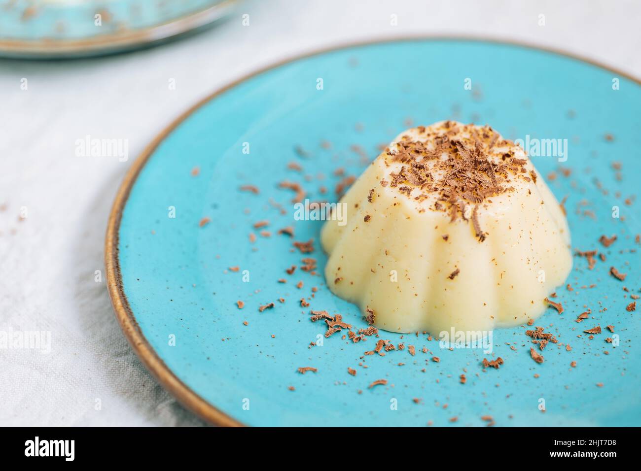 Vanillepudding auf blauem Porzellanteller mit Schokoladenbröseln darauf. Heller Hintergrund Stockfoto