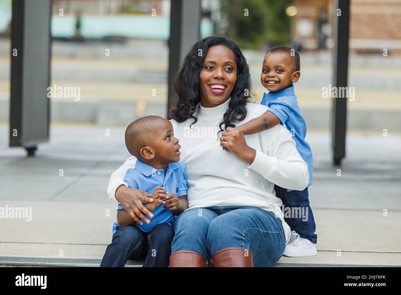 Eine Mutter mit langen Haaren sitzt draußen mit ihren beiden kleinen Söhnen Stockfoto