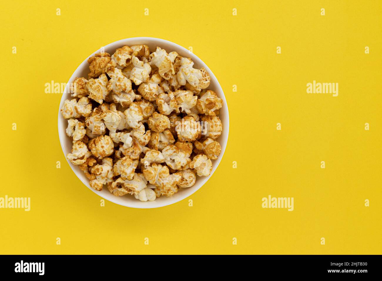 Karamell-Popcorn in einer Schüssel auf Gelb mit Platz für Text, Nahaufnahmen, süße Snacks und Karamell-Popcorn zum Ansehen von Filmen Stockfoto