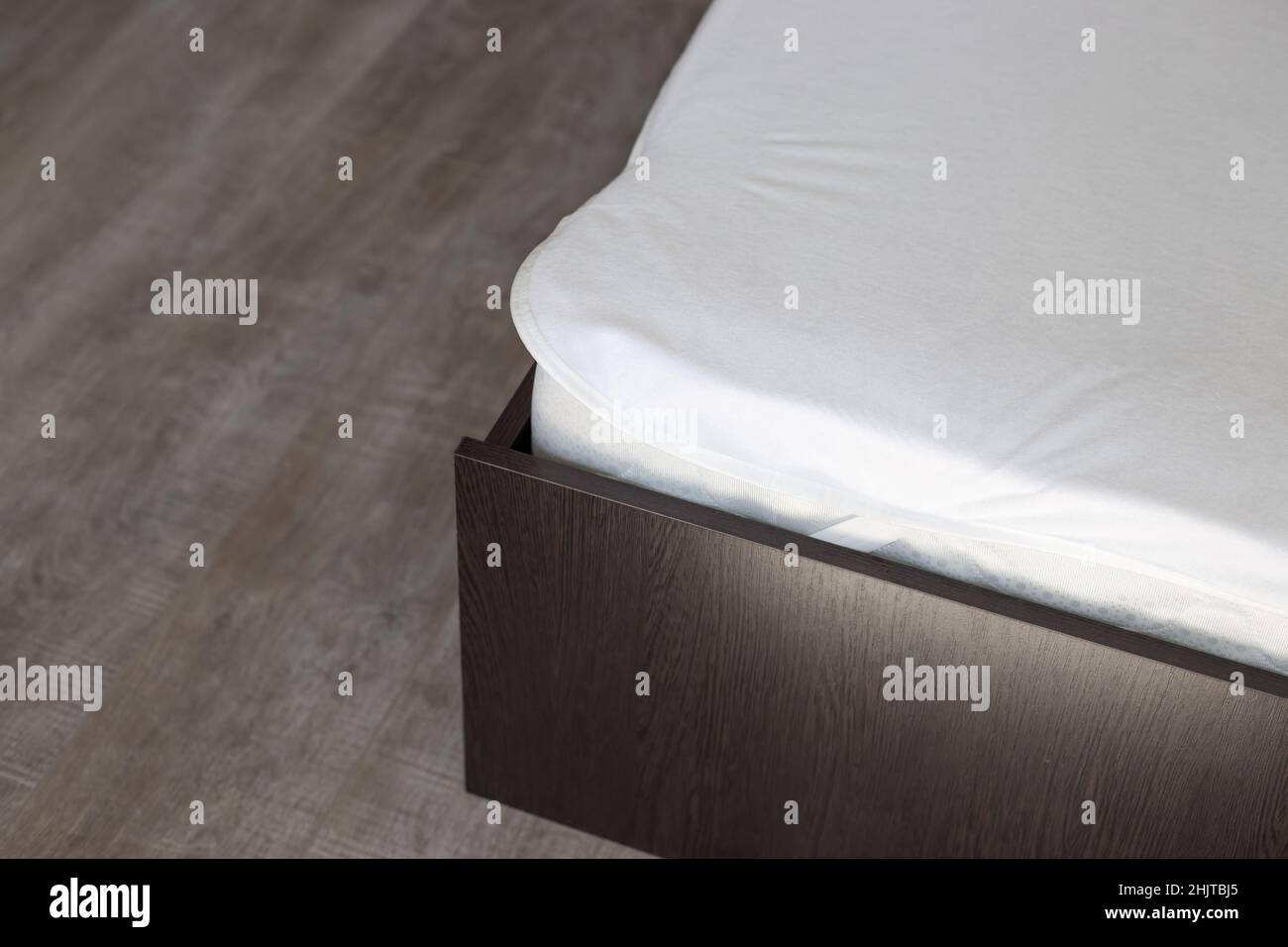 Bettecke aus Holz mit Polyurethan-Matratze und wasserdichter weißer Abdeckung. Pflege der Schlafzimmermöbel. Stockfoto