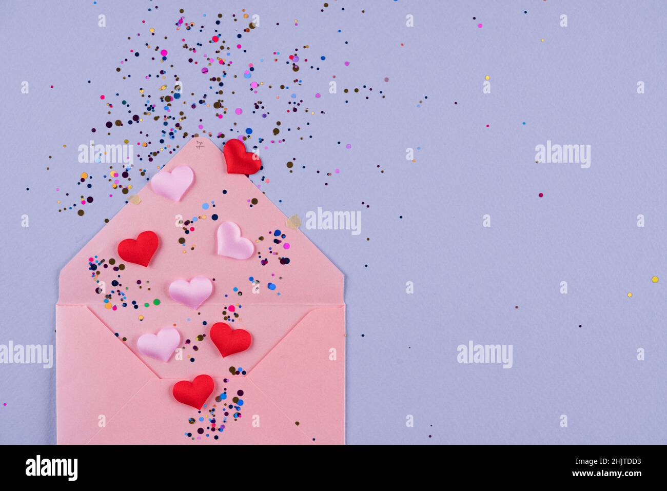 Valentinstag festlichen Hintergrund. Pinkfarbener Umschlag mit roten Herzen und Konfetti-Umschlägen auf trendigem violettem Hintergrund mit Kopierfläche. Flach liegend, Draufsicht Stockfoto