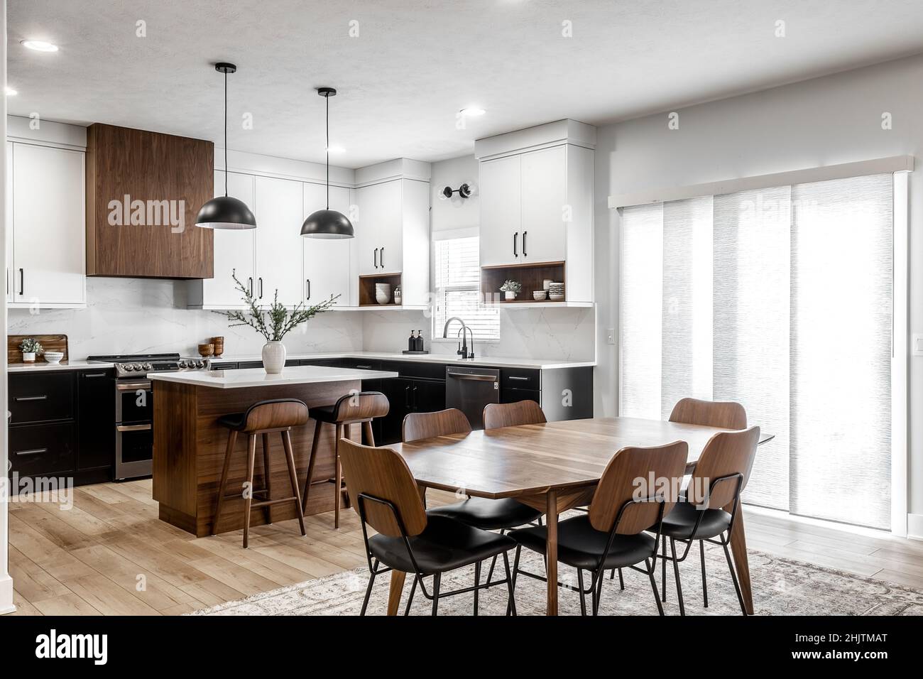 Moderne Küche und Esszimmer im mittleren Jahrhundert mit schwarzen Schränken, weißen Schränken, weißen Quarz- und Walnussakzenten Stockfoto