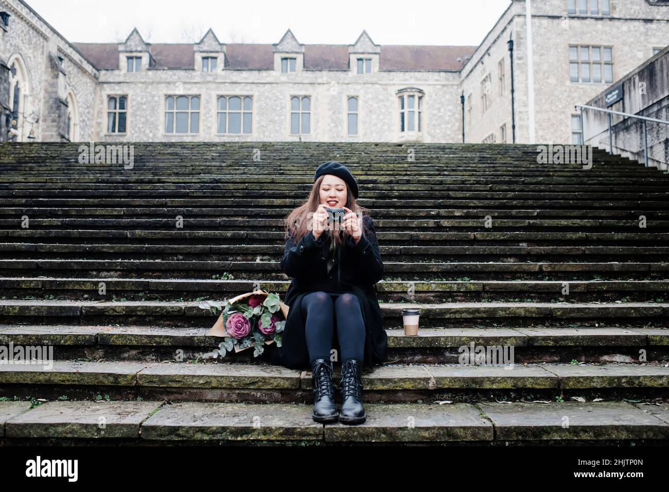Asiatin saß auf den Stufen und fotografierte in Winchester, Großbritannien Stockfoto