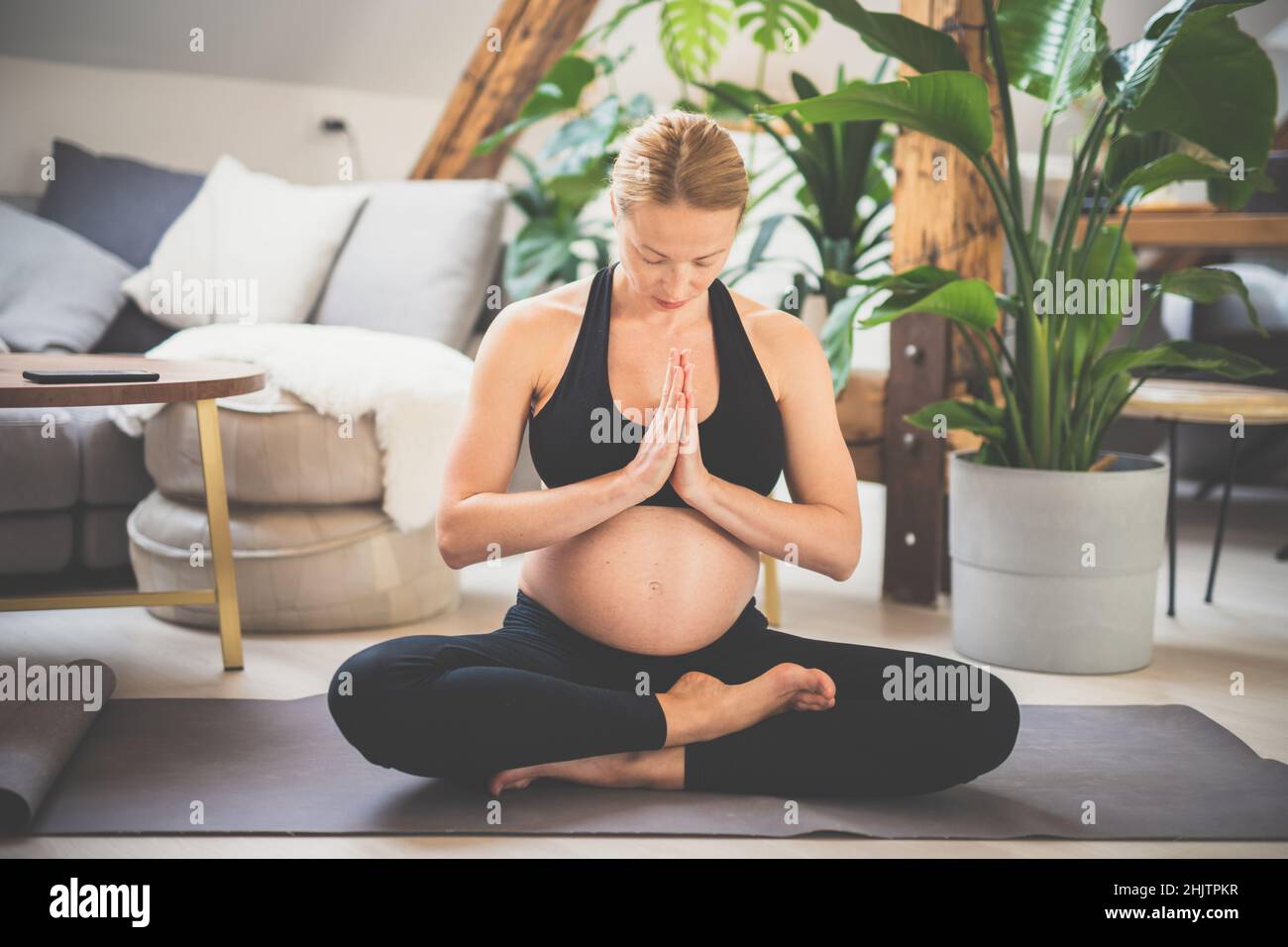 Junge schöne Schwangerin, die zu Hause in ihrem Wohnzimmer Yoga trainiert. Mutterschaft, Schwangerschaft, gesunder Lebensstil und Yoga-Konzept Stockfoto