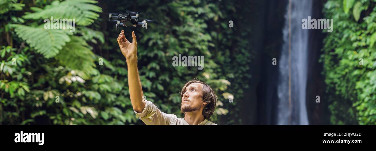 Der Mann steuert die Drohne vor dem Hintergrund des Waldes und dem Wasserfall-BANNER, LANGFORMATIG Stockfoto
