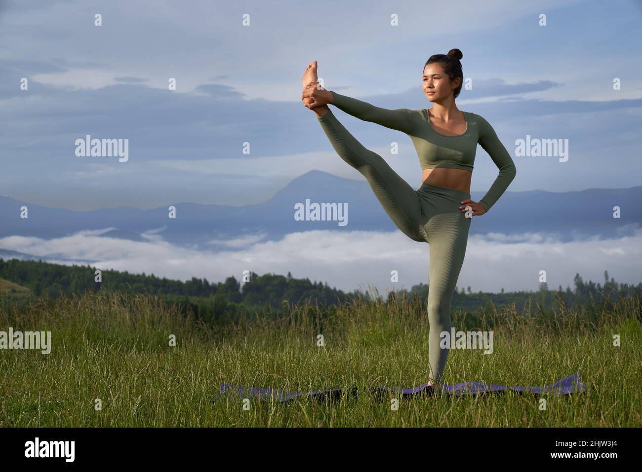 Sportliche junge Frau im aktiven Ohr, die Yoga-Übungen mit Bergen im Hintergrund macht. Eine gesunde und fit Frau, die im Sommer draußen trainieren kann. Stockfoto
