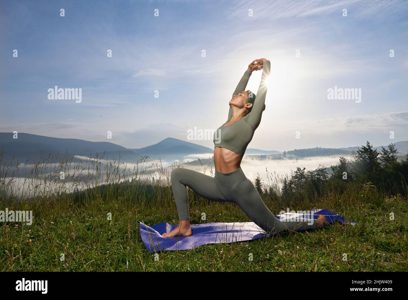 Gesund fit Frau mit schlankem Körper tun Yoga-Übungen zwischen grünen Sommer Berge. Hübsche Dame mit dunklem Haar, die morgens Zeit für ein aktives Training verbringt. Stockfoto