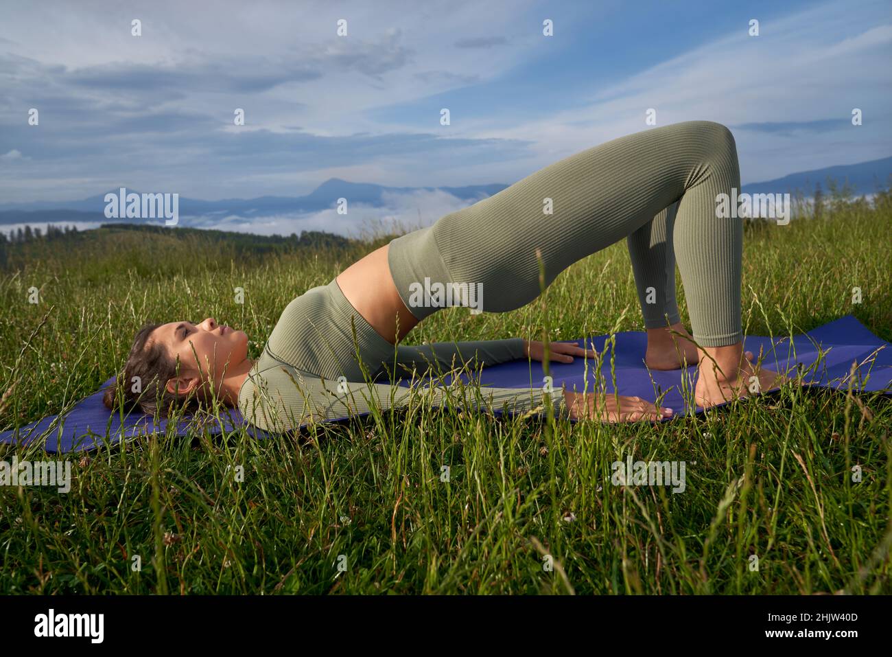 Schöne junge Frau mit schlankem Körper verbringen Freizeit für Outdoor-Training. Eine gesunde, fliegende Dame liegt auf einer Yogamatte und macht Übungen für den Rücken. Stockfoto