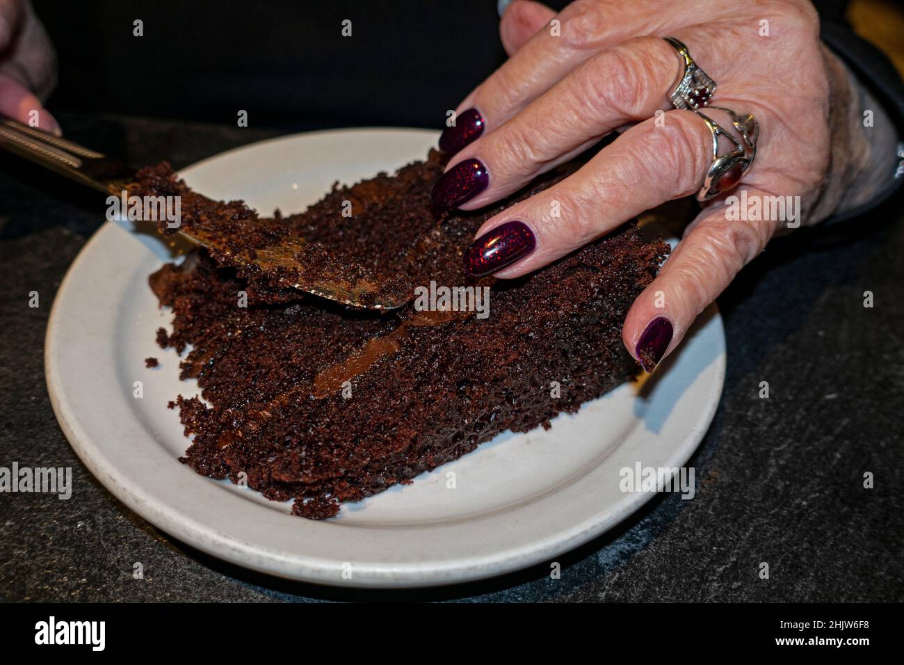 Dekadente Schokoladenkuchen, die im gehobenen Cafe Latte serviert werden und von einer Frau mit kastanienbraunen Nägeln mit roten Flecken geschnitten werden. St. Paul Minnesota, USA Stockfoto