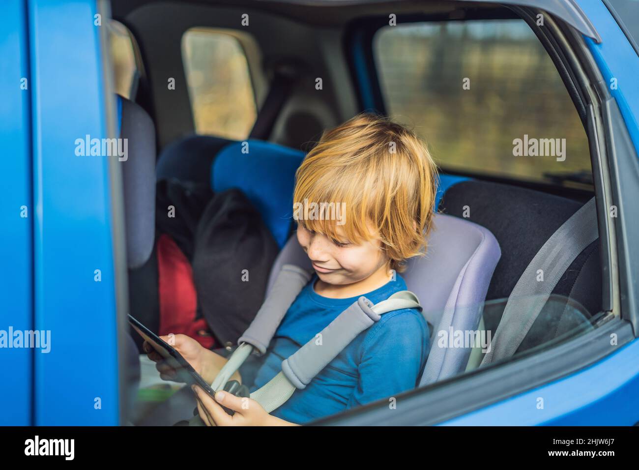 Kleiner Junge auf dem Rücksitz eines Autos mit Hilfe der Kontaktschaltertafel selbst während der Fahrt zu unterhalten Stockfoto