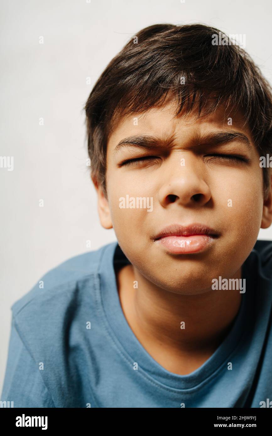 Angespannter indischer Junge mit geschlossenen Augen auf weißem Hintergrund. Nahaufnahme. Er trägt ein einfaches Baumwollhemd Stockfoto