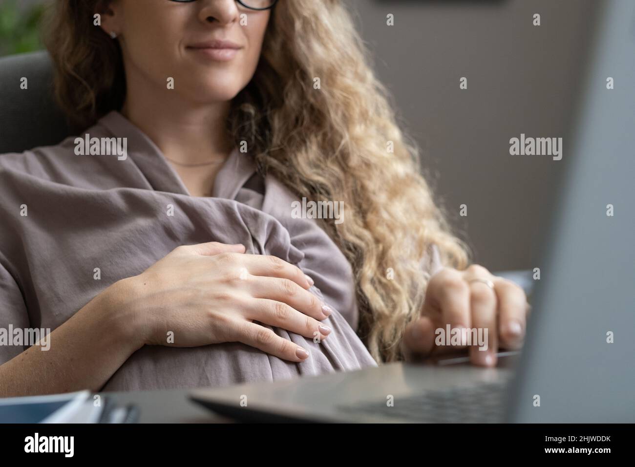 Schwanger Geschäftsfrau in schickem Kleid berühren ihren Bauch und Networking vor dem Laptop, während sie am Schreibtisch sitzen Stockfoto