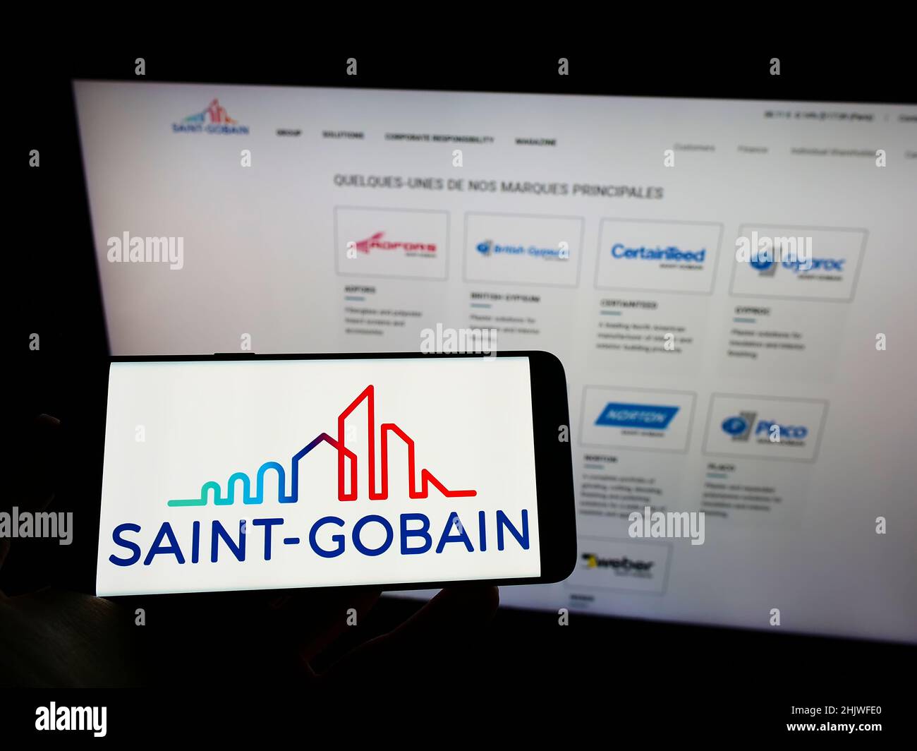 Person mit Mobiltelefon und Logo der französischen Compagnie de Saint-Gobain SA auf dem Bildschirm vor der Webseite. Konzentrieren Sie sich auf die Telefonanzeige. Stockfoto