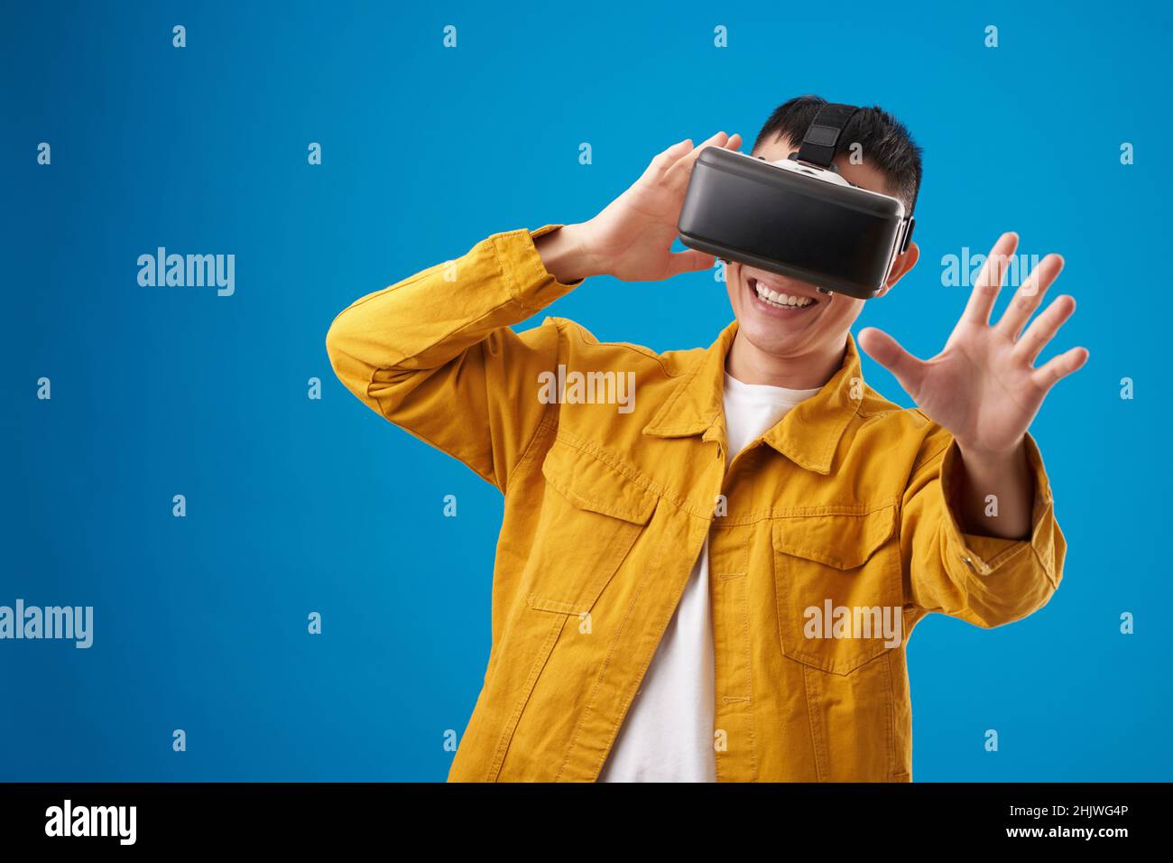 Positiver junger Mann testet neue Anwendung für Virtual-Reality-Headsets, isoliert auf Blau Stockfoto