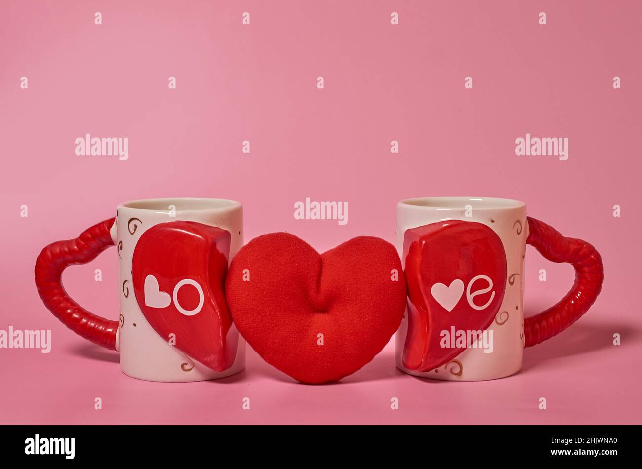 Zwei paarige Tassen mit der Aufschrift Love und einem roten Plüschherz dazwischen Stockfoto