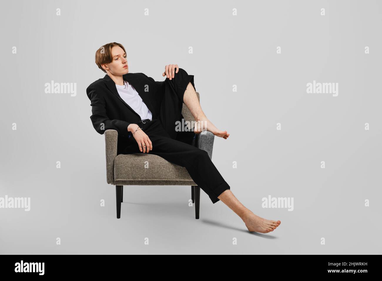 Junger Barfußmann im schwarzen Anzug, der im Sessel im Studio sitzt Stockfoto
