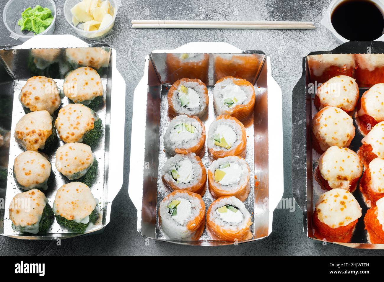 Sushi-Brötchen zum Mitnehmen in Behältern, philadelphia-Brötchen und gebackene Garnelenrollen auf grauem Steinhintergrund Stockfoto