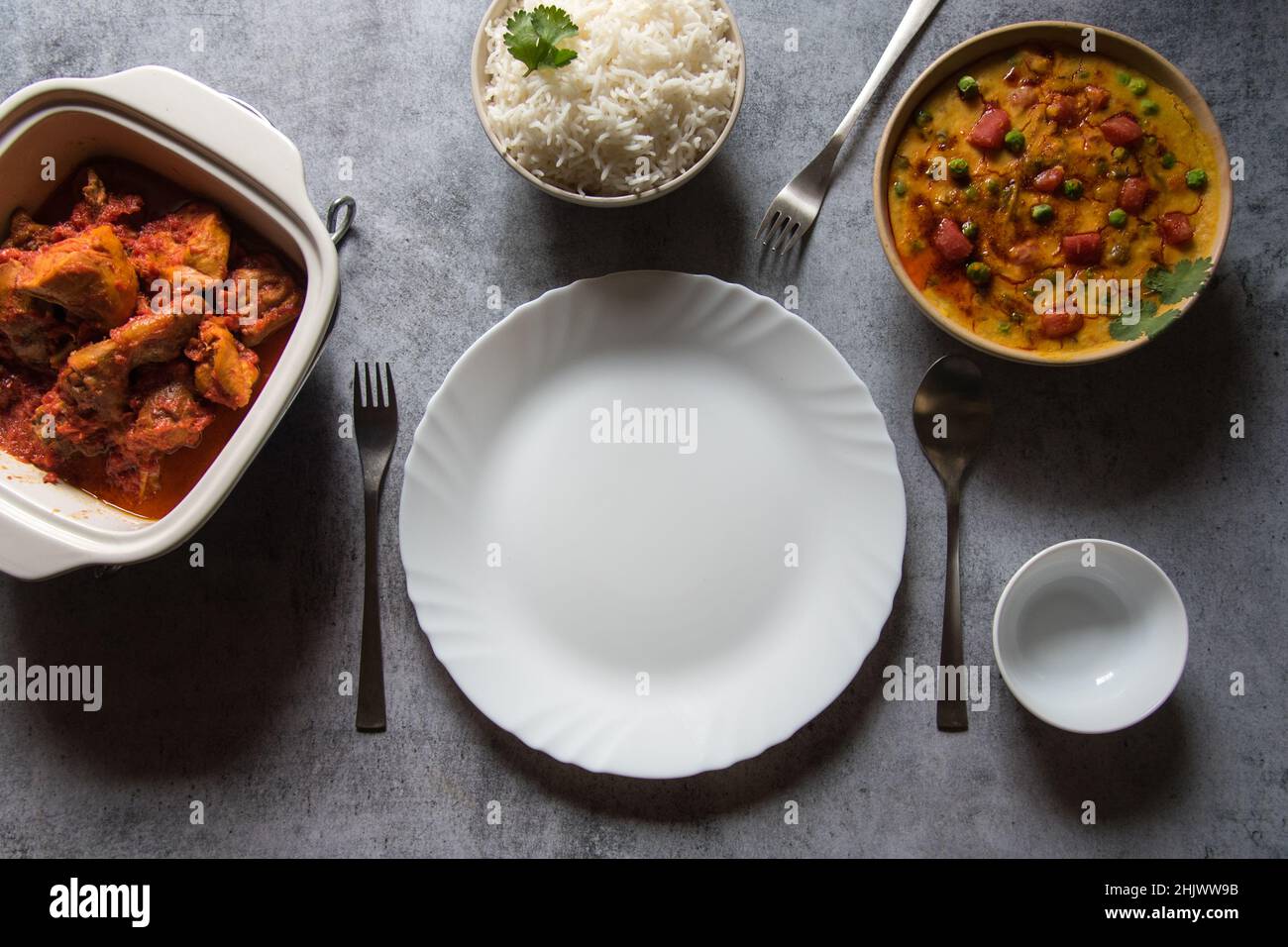 Leerer Teller auf einem Hintergrund zusammen mit gekochten Speisen, die serviert werden sollen. Stockfoto
