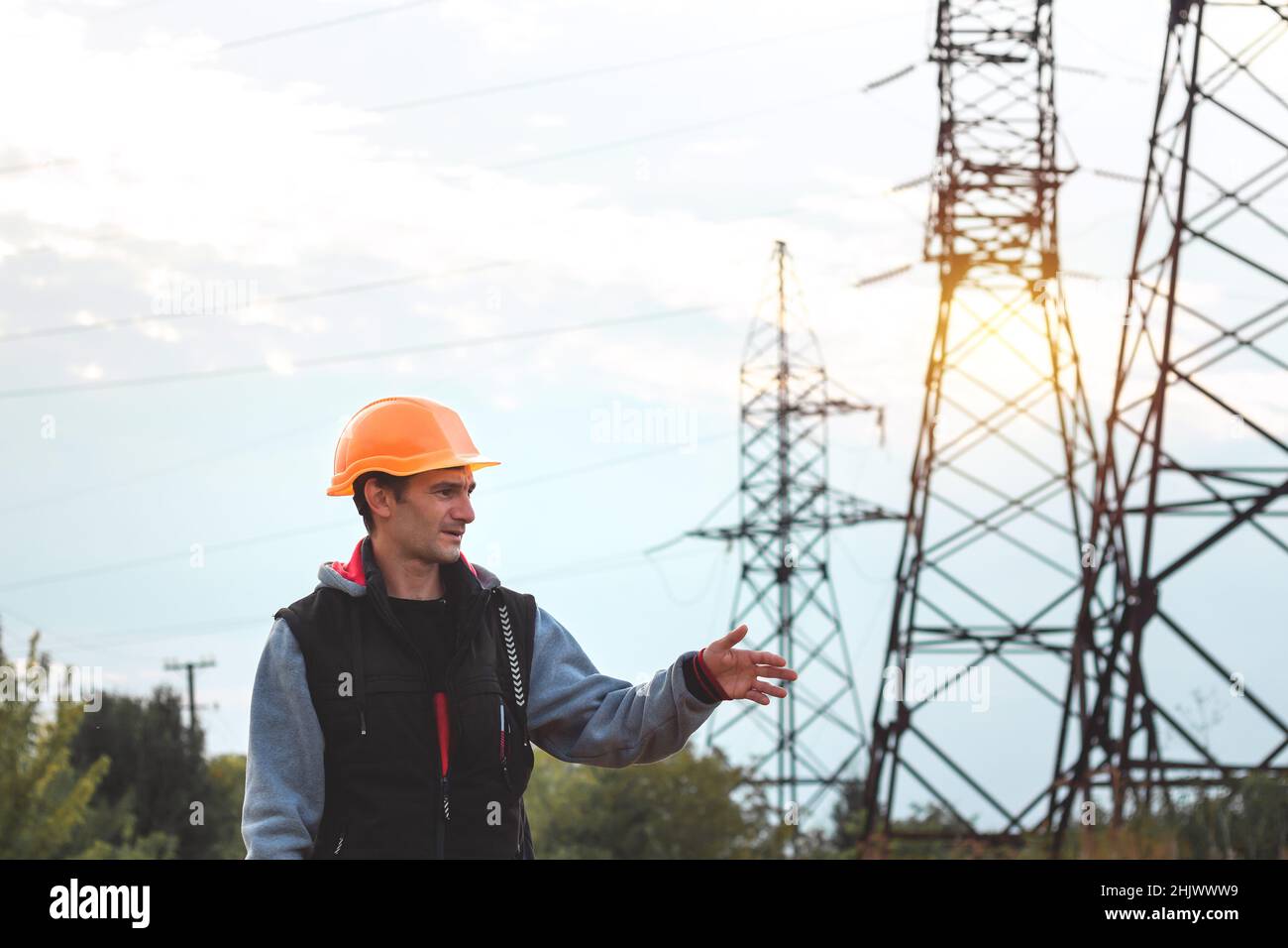 Arbeiter in einem Helm vor dem Hintergrund eines Umspannwerks und Hochspannungsmasten Stockfoto