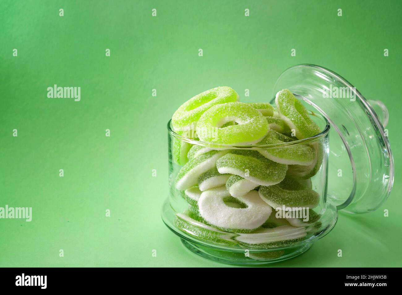Kaubonbons und Gummy-Candy-Konzept mit Apfelgeschmack mit Nahaufnahme von süßen und sauren grünen Ringen, die mit granuliertem Zucker in einem durchsichtigen Glas mit Isol bedeckt sind Stockfoto