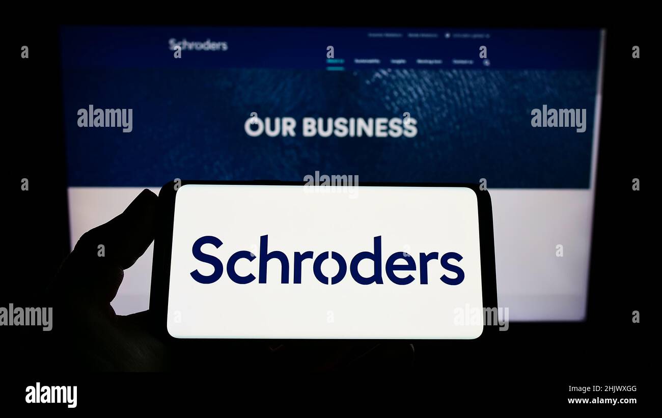 Person, die ein Smartphone mit dem Logo des britischen Vermögensverwaltungsunternehmens Schroders plc auf dem Bildschirm vor der Website hält. Konzentrieren Sie sich auf die Telefonanzeige. Stockfoto