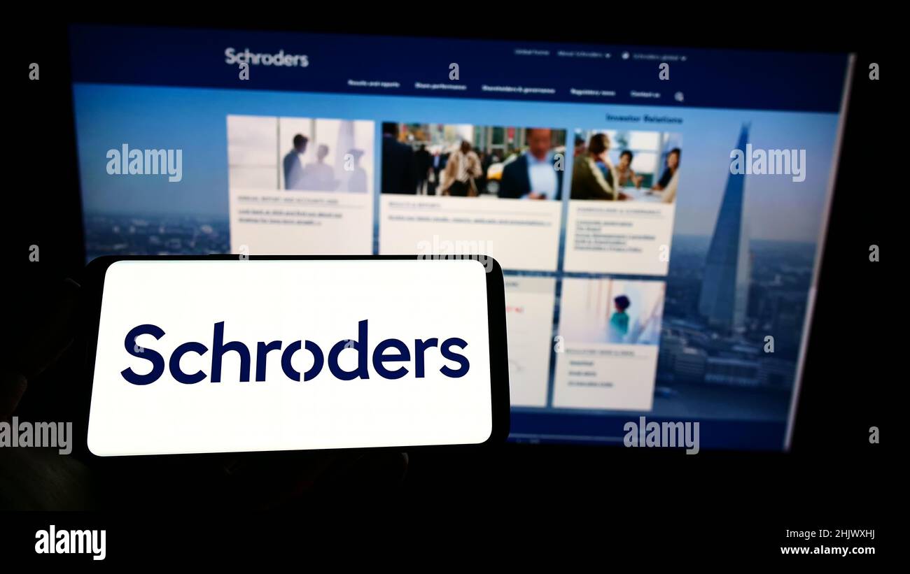 Person mit Mobiltelefon und Logo des britischen Vermögensverwaltungsunternehmens Schroders plc auf dem Bildschirm vor der Webseite. Konzentrieren Sie sich auf die Telefonanzeige. Stockfoto
