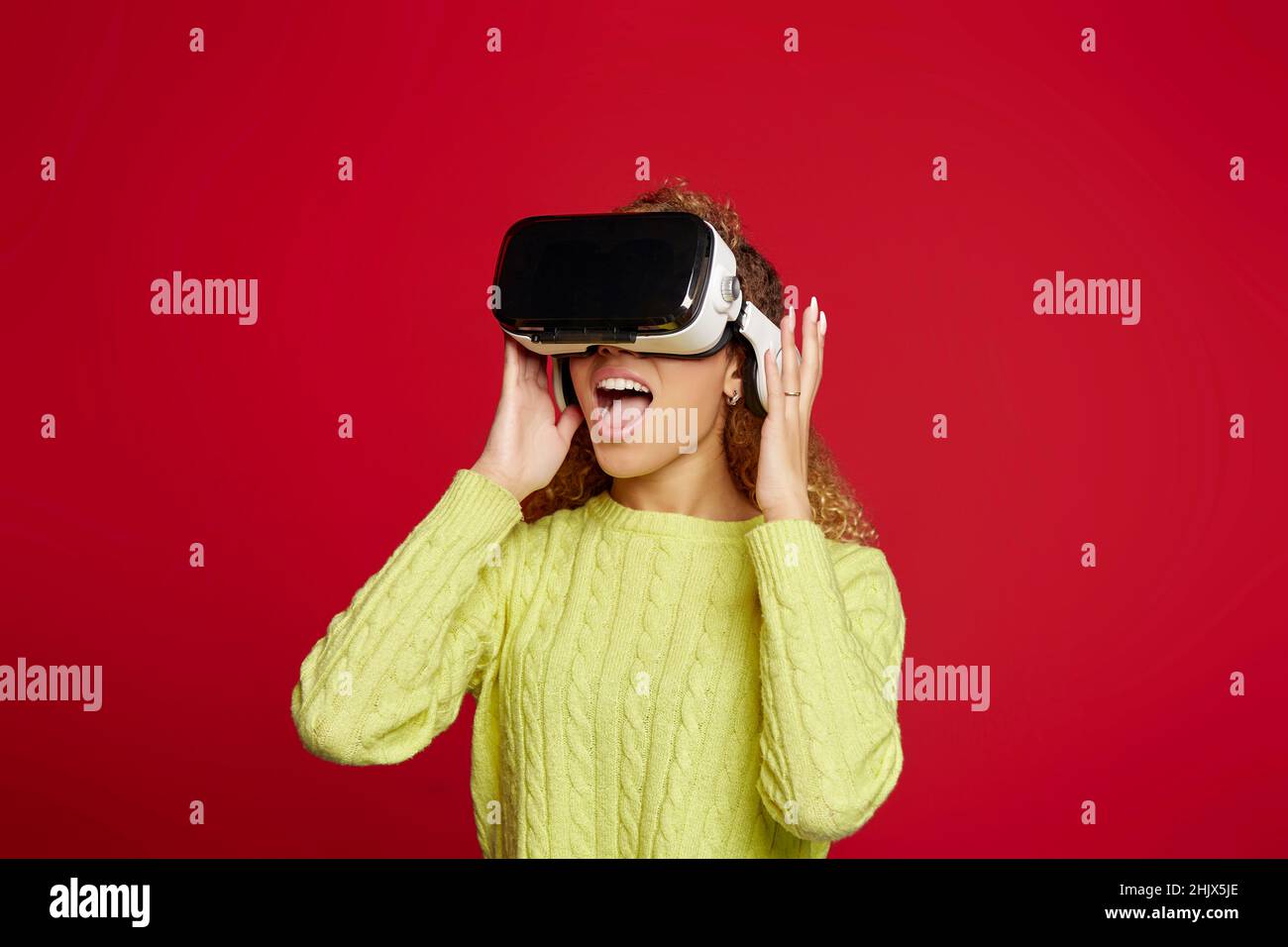 Erstaunte afroamerikanische Frau in einer Brille der virtuellen Realität, die den Cyberspace auf rotem Hintergrund im Studio erkundet Stockfoto