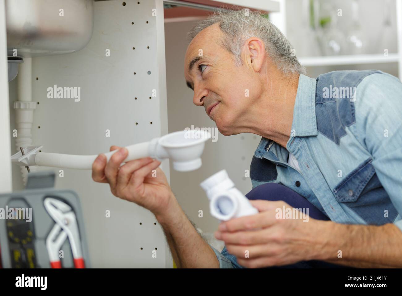 Senior Klempner Befestigung unter dem Waschbecken in der Küche Stockfoto