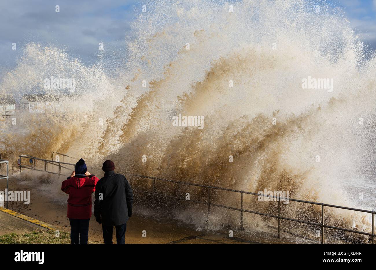 Ein Paar fotografiert spektakuläre Wellen bei Flut, die an der Strandpromenade am Southwold Pier stampfen Stockfoto