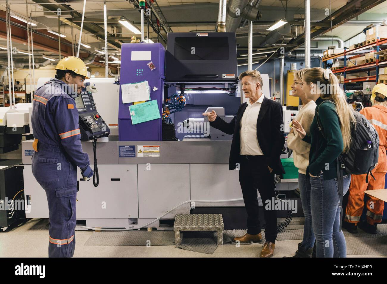 Geschäftsmann und Familie diskutieren mit männlichen Arbeitern, während sie bei der Herstellung von Maschinen in der Fabrik stehen Stockfoto