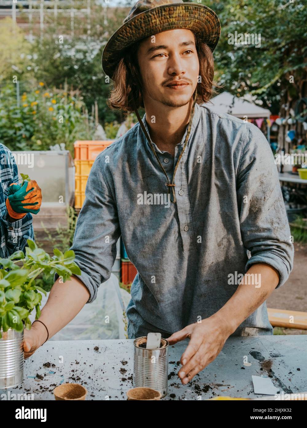 Junger Bauer mit Pflanze, die im Gemeinschaftsgarten wegschaut Stockfoto