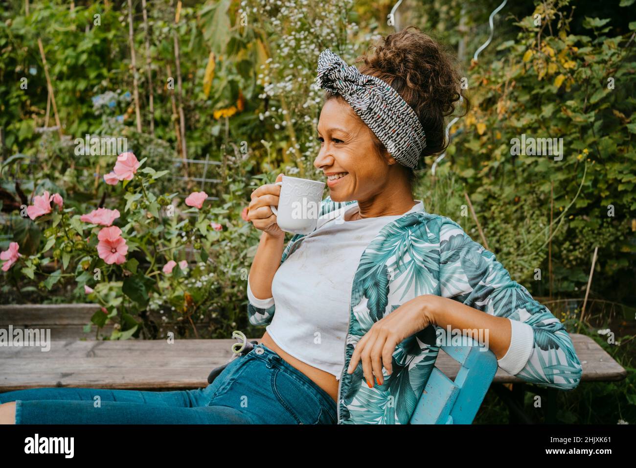 Lächelnde Bäuerin, die Kaffee trinkt, während sie auf der städtischen Farm sitzt Stockfoto