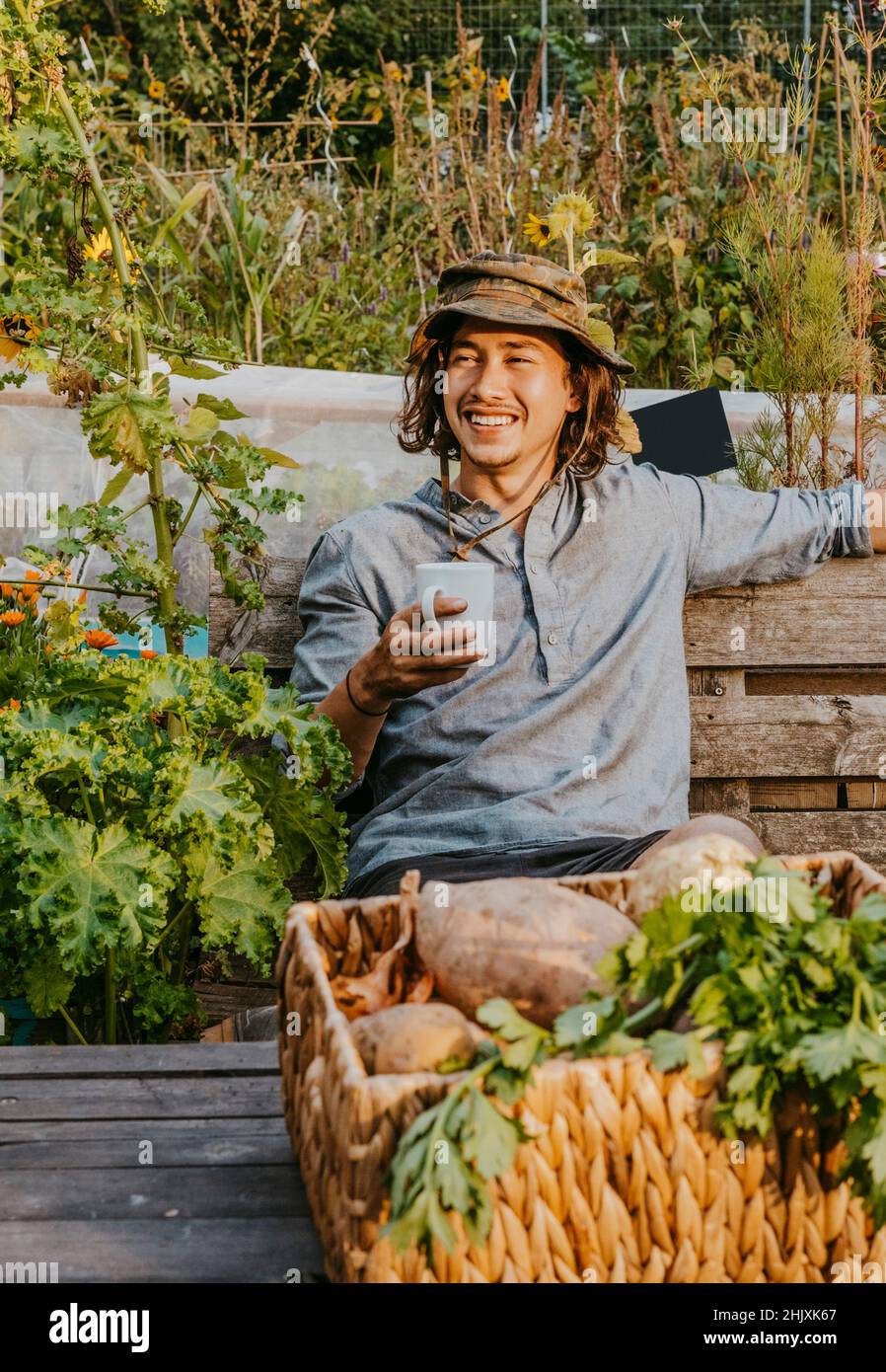 Lächelnder Bauer mit Kaffeetasse auf der Bank auf dem Bauernhof Stockfoto