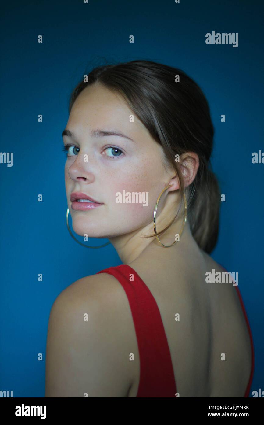 Brunette Mädchen posiert gegen eine blaue Wand trägt rote Spitze und Reifen Ohrringe. Stockfoto