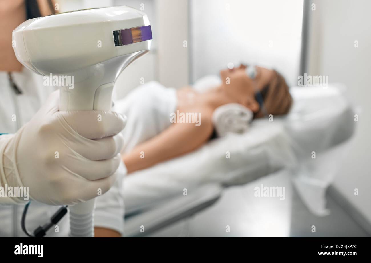 Kosmetikerin, die das Lumecca-Gerät mit der IPL-Technologie für intensives gepulstes Licht hält, um den Körper einer Frau zu fotorejuvenieren und braune Flecken und Flecken zu entfernen Stockfoto