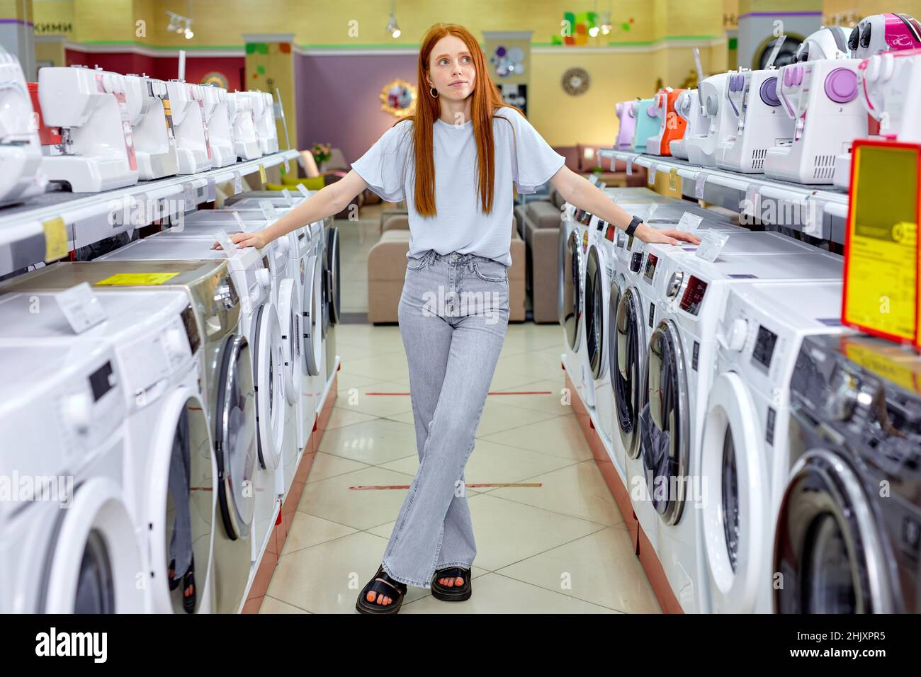Gut aussehende Dame im lässigen Outfit stehen bei neuen Waschmaschinen, Make-Kauf, neues Waschgerät. Kaukasische Dame mit langen roten Haaren wählen, ne Stockfoto
