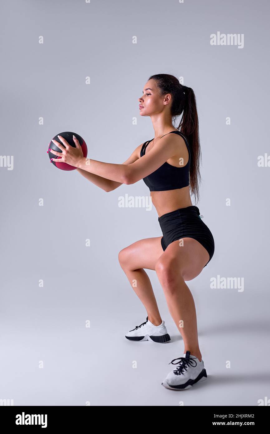 Seitenansicht Porträt von Slim Caucasian Cross fit Frau mit Fitness-Ball hockt, isoliert im Studio. Fit Lady trainiert mit Medizinball. Koac Stockfoto